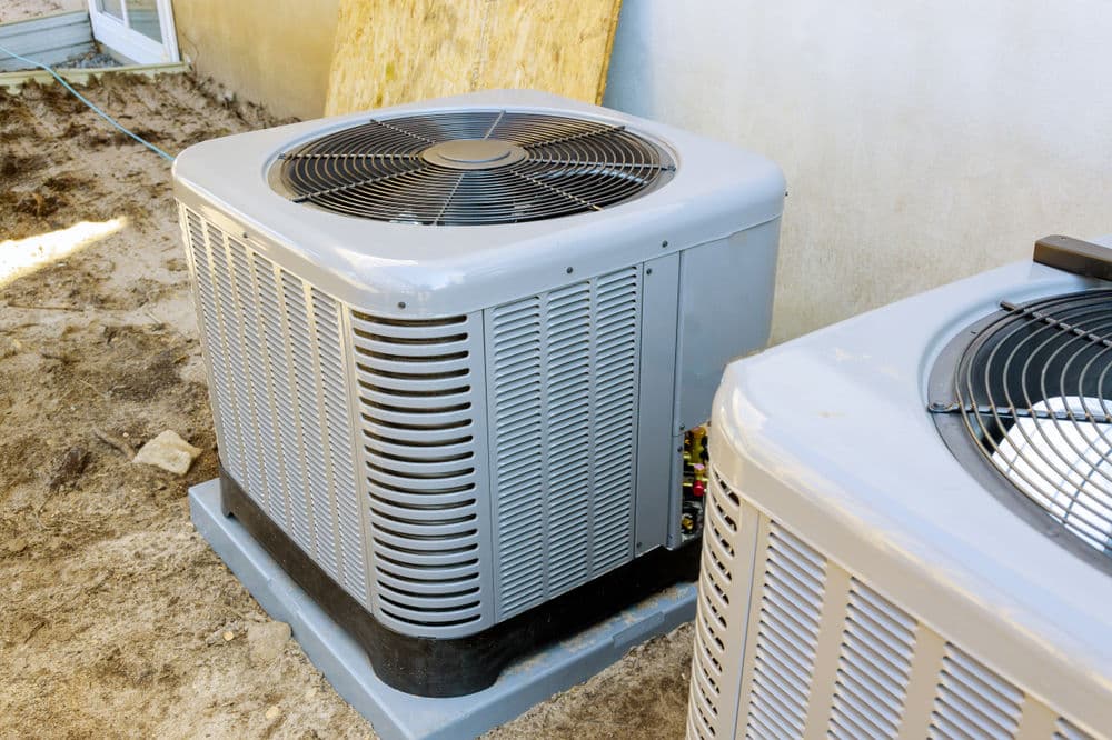 Air conditioning unit outside a building, showcasing its fan and metal construction on the ground.
