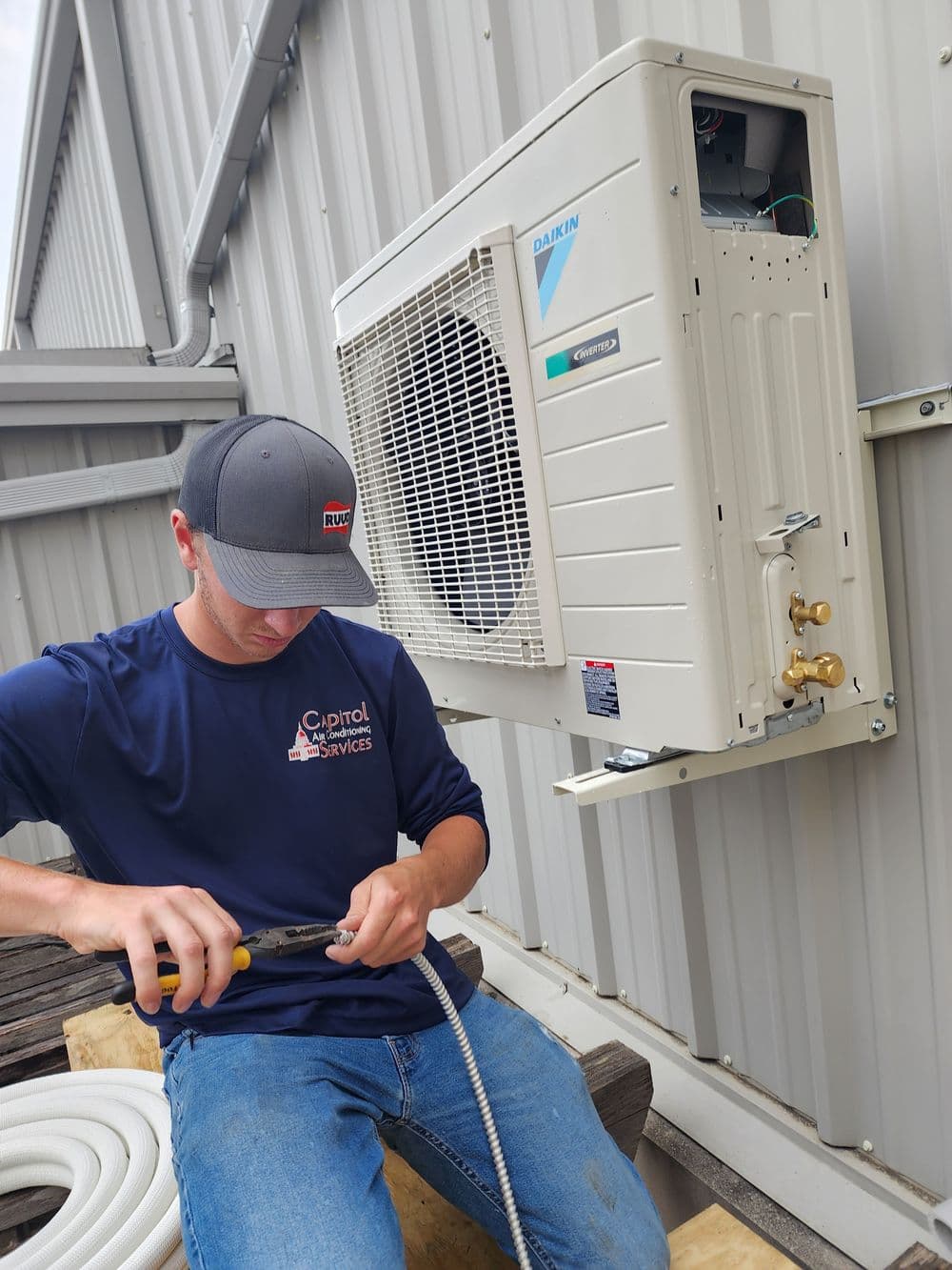 Technician repairing a Daikin air conditioning unit on a building exterior.