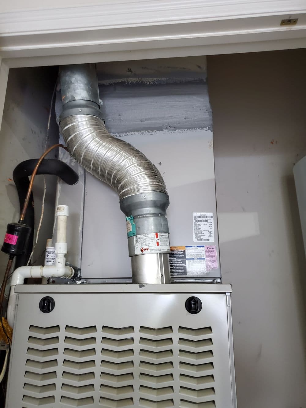 Furnace with venting system in a utility closet, showcasing exhaust and plumbing details.