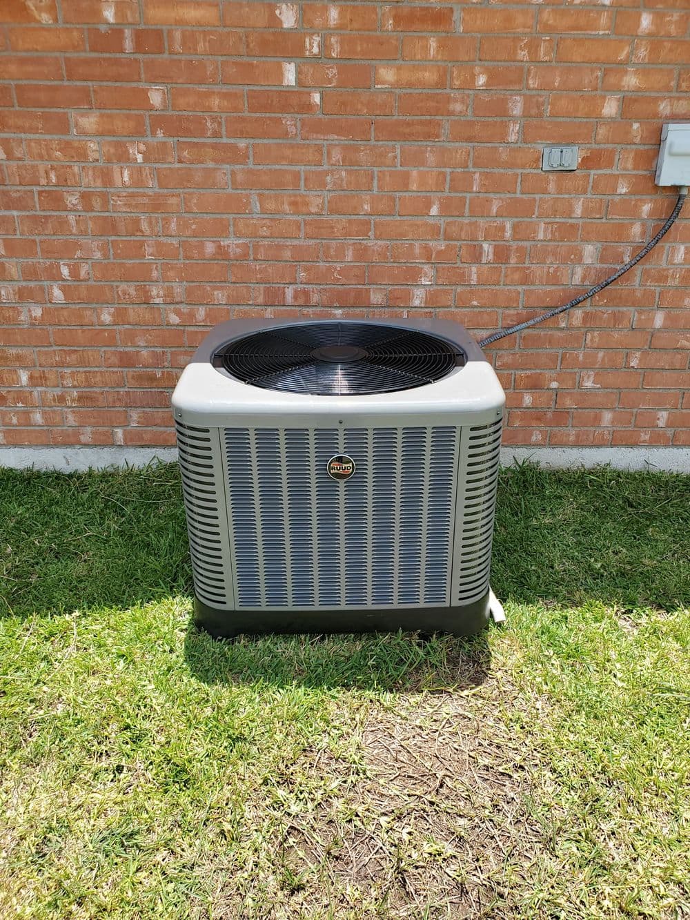 Air conditioning unit on grass near a brick wall, ideal for home cooling solutions.