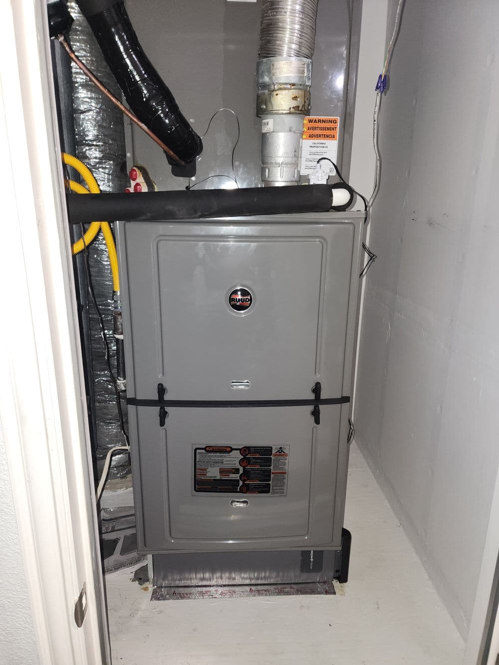 Modern gray furnace installed in a utility room with ducts and warning signs visible.