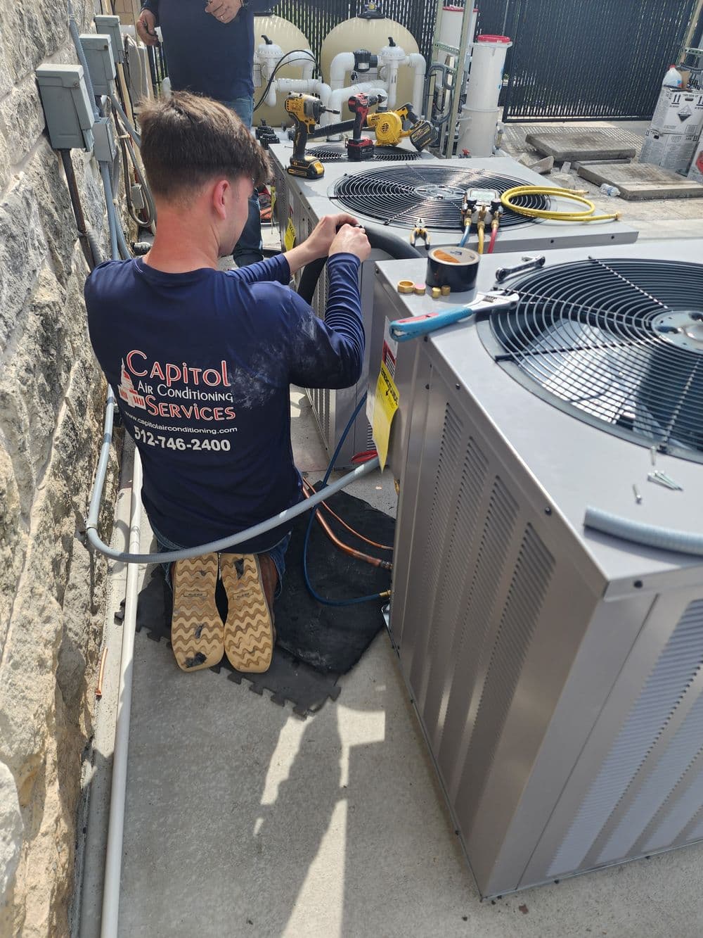 Technician servicing air conditioning units outdoors at Capitol Air Conditioning Services.