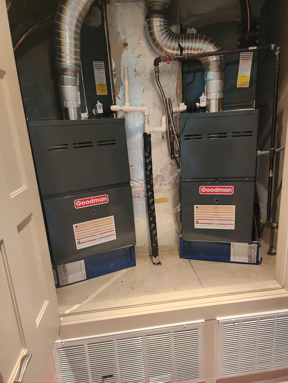 Goodman HVAC units installed in a utility closet with ductwork and plumbing visible.