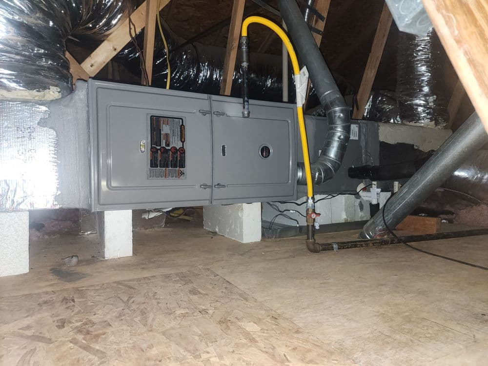 HVAC system installed in attic with insulated ducts and pipes on wooden flooring.