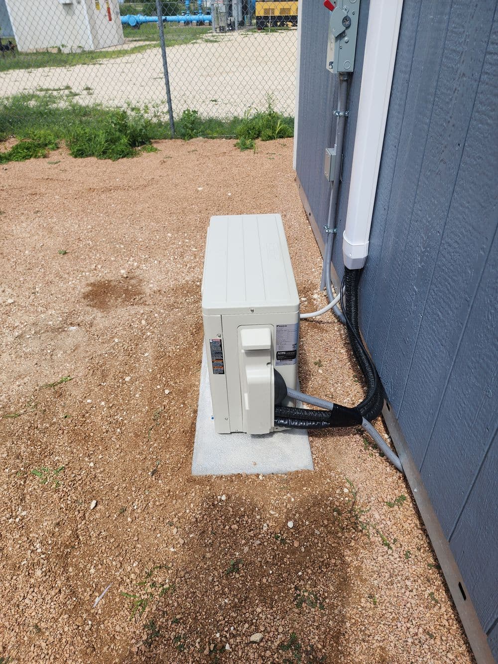 Air conditioning unit installed outside a building on a concrete slab, with visible connections.
